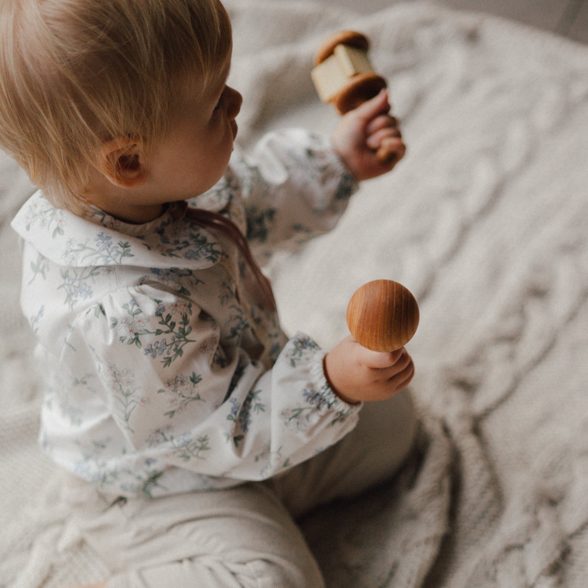 Baby sitting on a textured blanket holding wooden toys