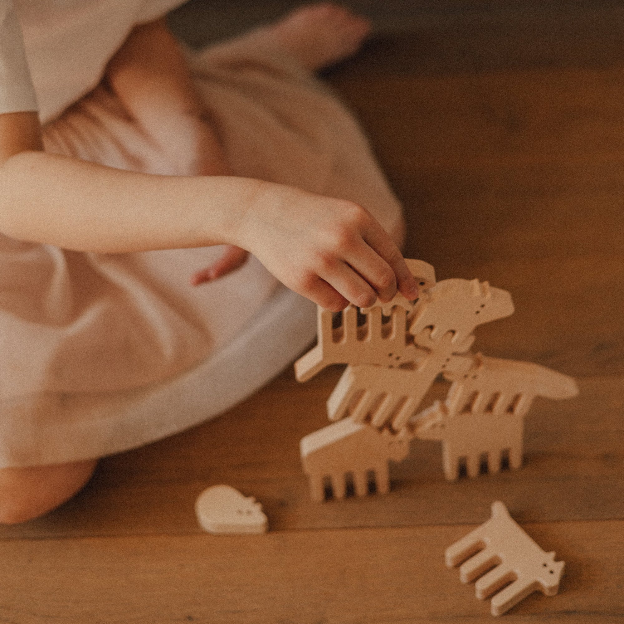 Child playing with wooden animal toys on a wooden floor