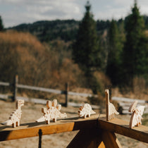 Wooden dinosaur toys on a wooden fence with a natural landscape in the background