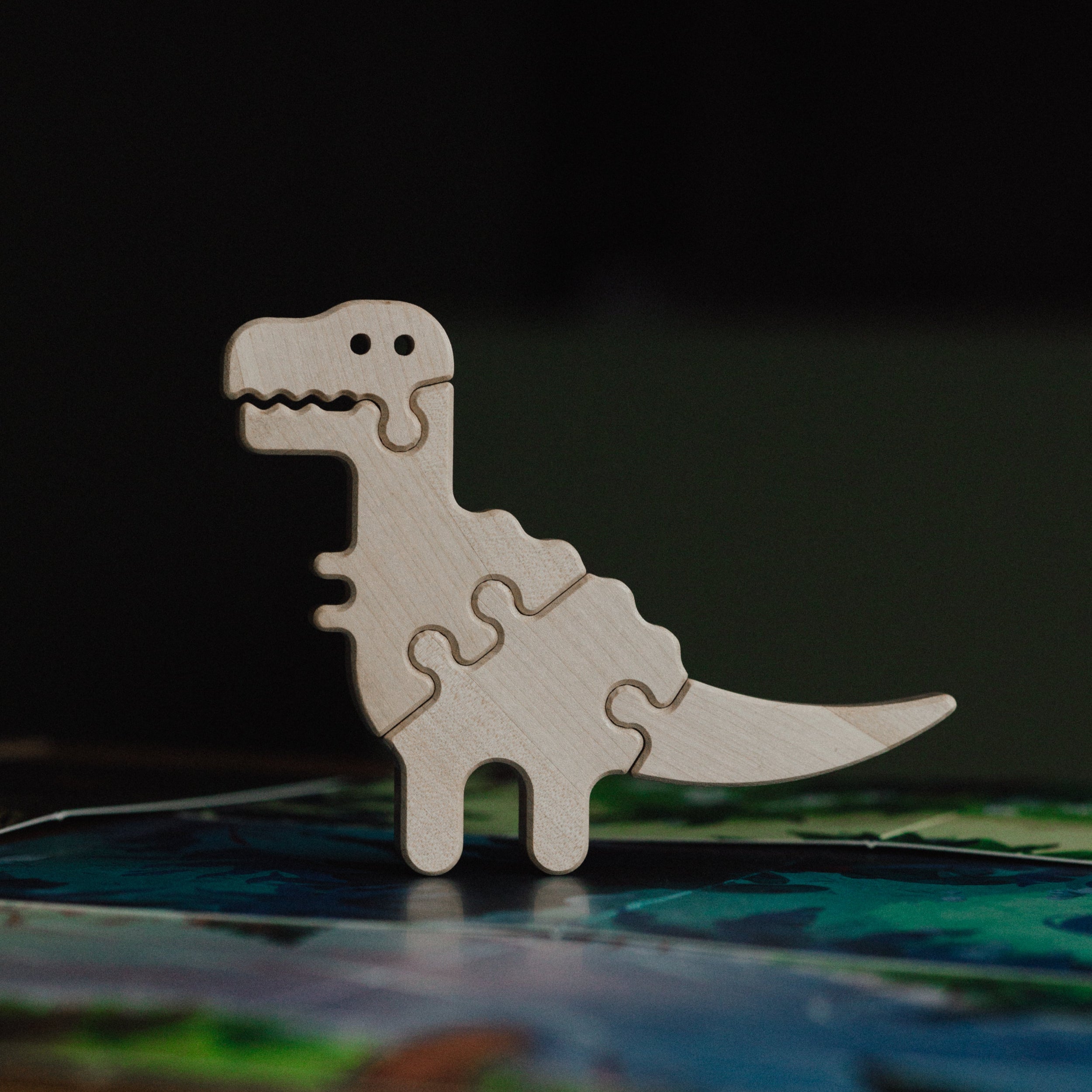 Wooden dinosaur puzzle piece on a colorful surface with a dark background