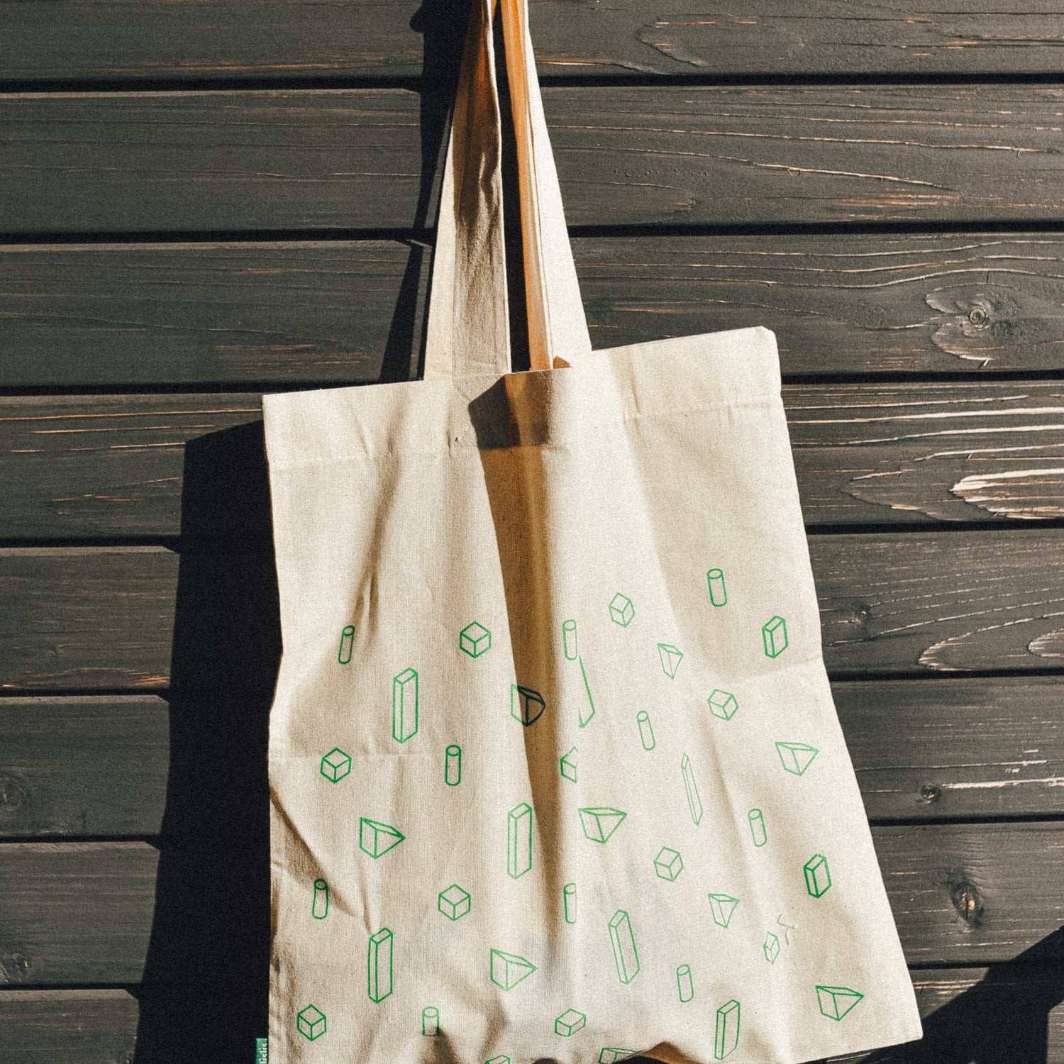 Beige tote bag with green patterns hanging on a wooden wall