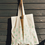 Beige tote bag with green patterns hanging on a wooden wall