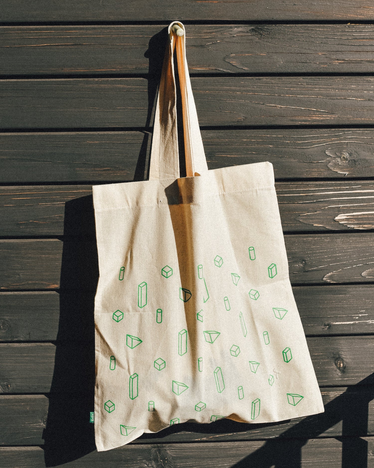 Beige tote bag with green patterns hanging on a wooden wall