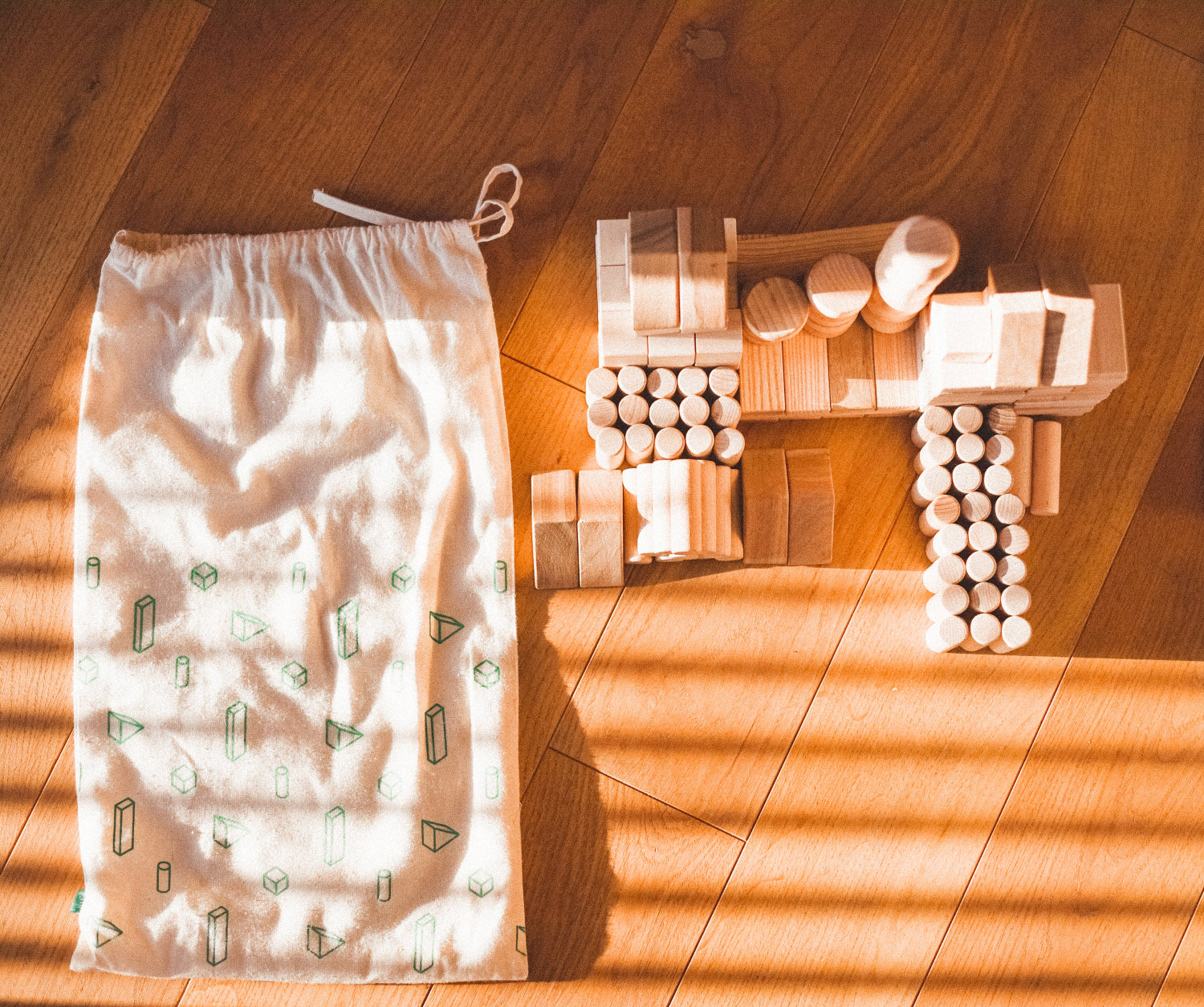 Wooden building blocks and a patterned drawstring bag on a wooden floor